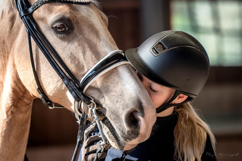Nahaufnahme von einem Mädchen, welches ihr blondes Pferd auf die Nase küsst
