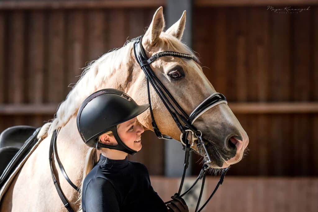 Portraitaufnahme von einer Reiterin mit ihrem blonden Barbiepferd auf Kandarre