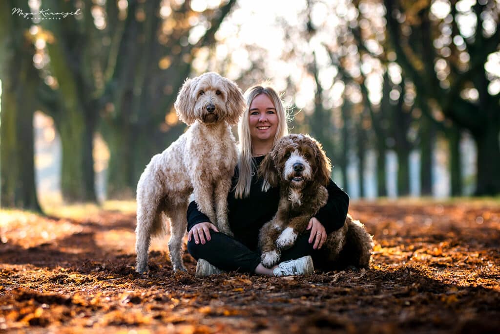 Fotografie von einer blonden Frau mit zwei Hunden auf einer Waldallee