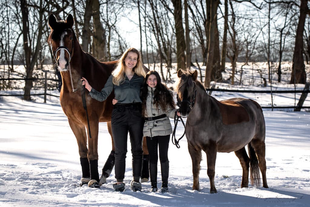 Zwei Schwestern mit ihren Pferden auf einer Winterwiese im Schnee