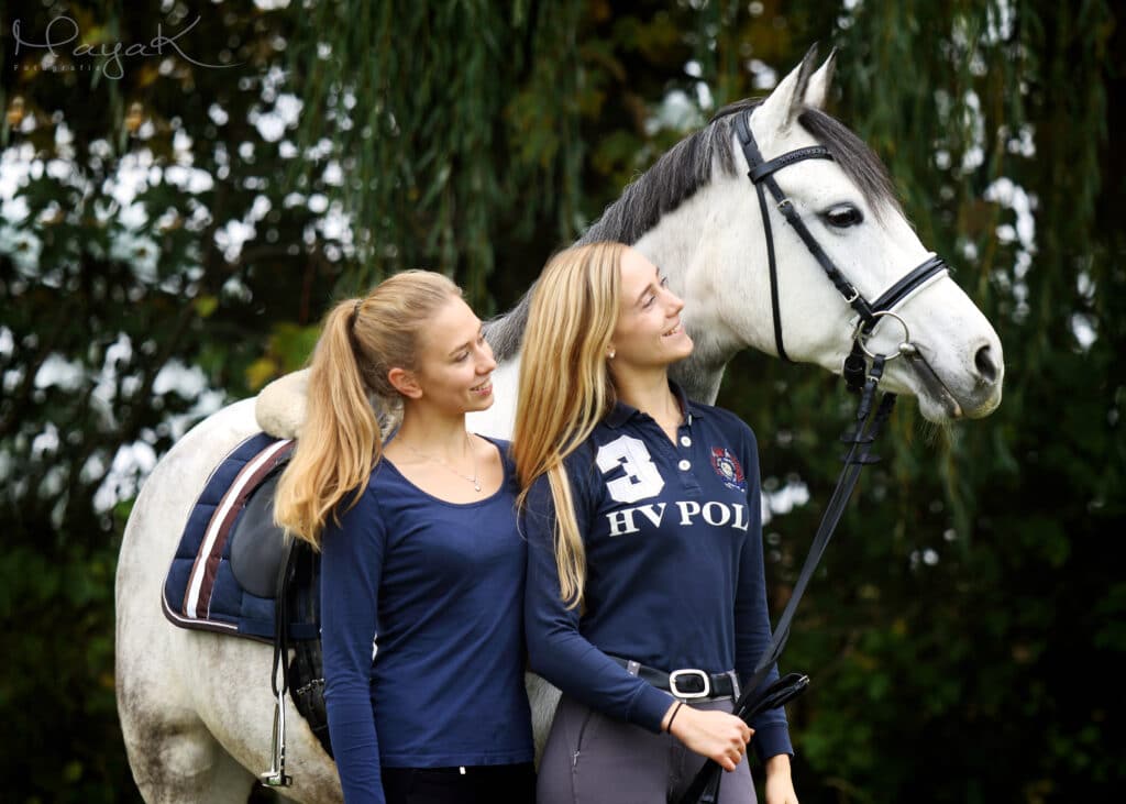 Zwei Geschwister Mädchen mit ihrer Schimmelstute im Wald