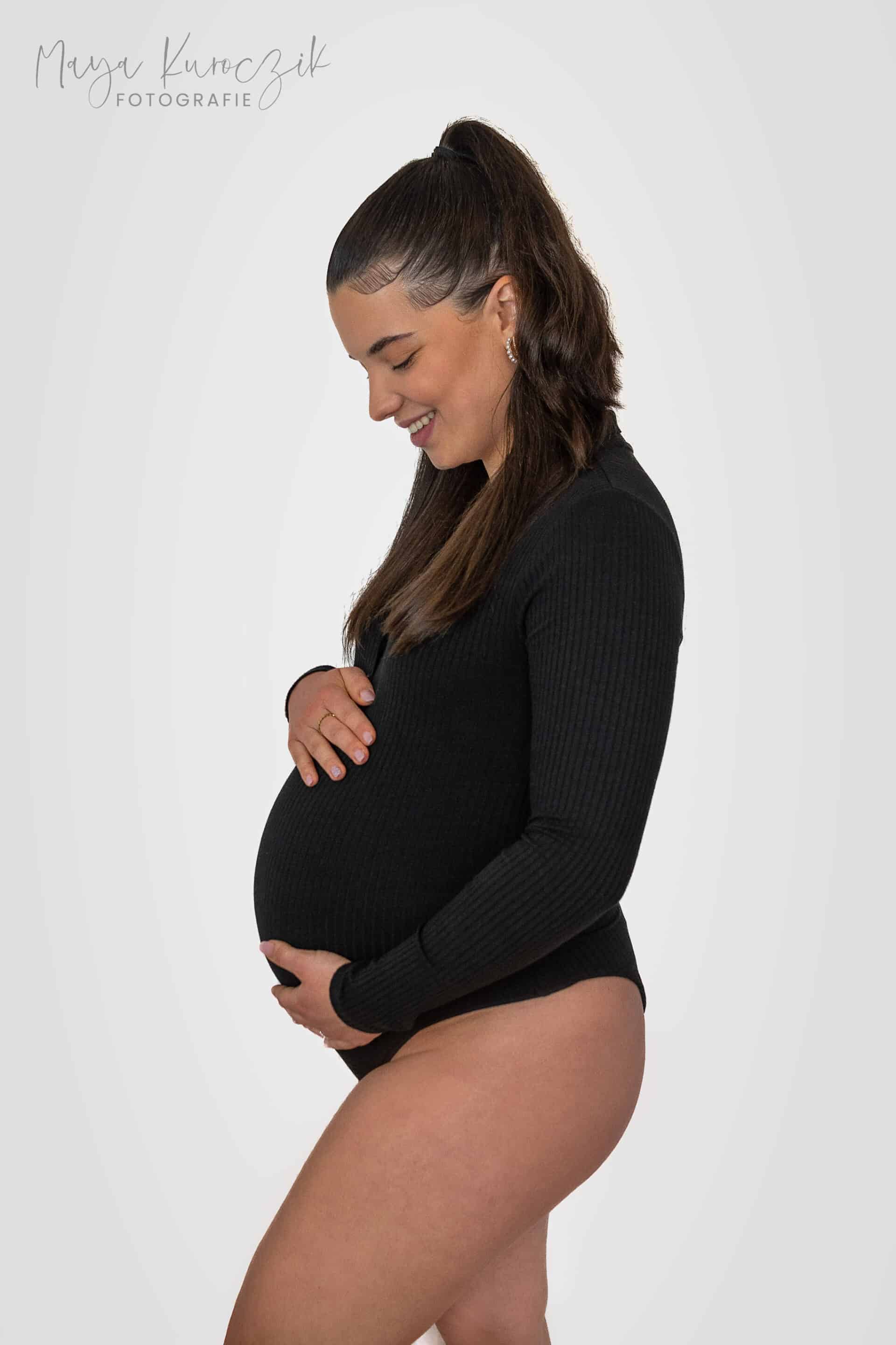 Schwangere Frau im schwarzen Body vor weißem Hintergrund